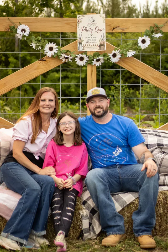 The Glitter Hooves family seated on a hay bale beneath a sunflower-draped photo arch