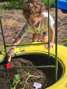 A child digging with a hand trowel in a yellow painted-tire garden bed
